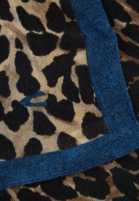 Leopardmønsteret stof med sorte og tan pletter, kantet med en solid blå accent. Blød tekstur med en let gennemsigtig kvalitet.