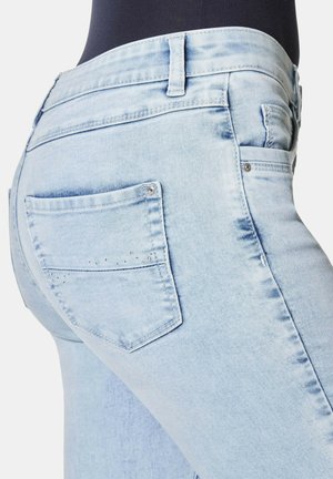 Helle blaue Jeans mit slim fit, die eine Gesäßtasche mit kleinen Nieten und einer glatten Textur aufweisen.