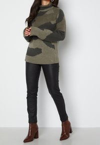 Maglione verde khaki con motivo camouflage nero, con orlo a costine e collo alto. Abbinato a pantaloni neri simili alla pelle e stivali lucidi marroni con tacco.