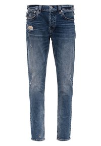 Vaqueros de mezclilla azul con un ajuste slim, que presentan parches gastados y desgastados en la parte superior del muslo izquierdo y pequeños desgarros dispersos.