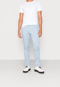 Ljusblå tajta byxor i ett mjukt material, kombinerat med en enkel vit t-shirt med kort ärm och vita skor med svarta sulor.