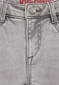 Pelēki džinsu bikses ar pogu aizdari, izteiksmīgu šuvju un tekstūru. Uz birkas lasāms "Jog Denim" sarkanā krāsā.