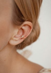 Orecchino a clip in oro con design a foglia e quattro gemme trasparenti. Vista ravvicinata che mostra l'orecchino posizionato sul lobo dell'orecchio.
