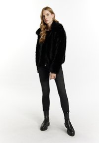 Sort imiteret pelsjakke med bred krave, båret over en sort top og skinny sorte jeans, parret med chunky sorte støvler.