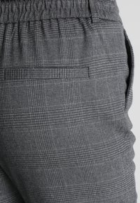 Grå rutiga byxor med elastisk midjeband, som har sidofickor och en passpoilerad bakficka, tillverkade av strukturerad tyg.