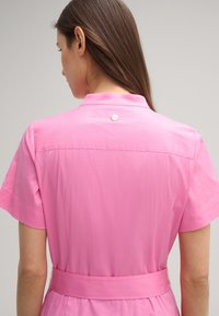 Rosa Kurzarmkleid mit Kragen, tailliertem Bund, glatter Textur und einem kleinen dekorativen Knopf auf der Rückseite.