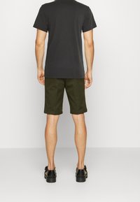 Černé tričko s krátkým rukávem, olivově zelené šortky a černé boty. Jednoduchý design, bavlněný materiál, s rovnými střihy a obšitými okraji.