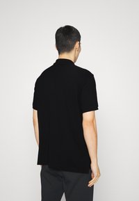 Black polo shirt with short sleeves, made of smooth fabric. Features a collar and a straight cut, shown from the back.