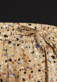 Sukně s elastickým pasem v béžové barvě s vícebarevnými tečkami. Obsahuje odpovídající stahovací šňůrku. Měkká, hladká tkanina s mírným leskem.