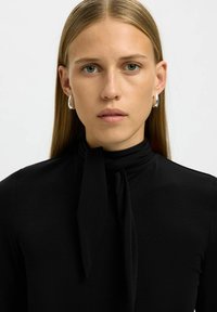 Zwarte langjarige top met een strikdetail bij de hals, een gladde textuur, een aansluitend ontwerp en een eenvoudige, klassieke silhouet.