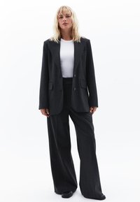 Mørkegrå stribet jakkesæt med en tætsiddende blazer med to knapper, parret med vide bukser og en hvid T-shirt med rund hals under.