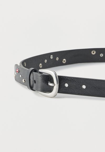 Μαύρη δερμάτινη ζώνη με ασημί πόρπη και μεταλλικά καρφιά, με πολλαπλές τρύπες ρύθμισης και μικρή κόκκινη πέτρα κοντά στην πόρπη.