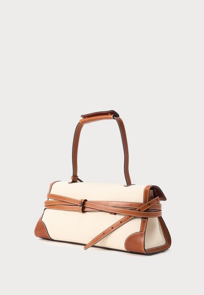Ορθογώνια μπεζ τσάντα χειρός με καφέ δερμάτινες λεπτομέρειες, διαγώνια ζώνη μπροστά και μονή πάνω λαβή σε απλό φόντο.