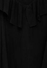 Schwarzer Stoff mit Rüsche entlang der oberen Kante und sichtbarer senkrechter Naht in der Mitte.