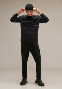 Felpa nera con strisce orizzontali in viola, blu e bianco; abbinata a pantaloni neri e scarpe chunky nere; indossa un berretto di maglia nero.