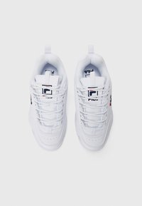 Une paire de baskets blanches FILA avec des lacets, un logo sur la languette et les côtés, vue d'en haut sur un fond blanc.
