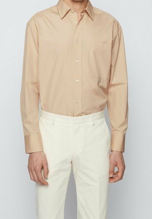 Beige overhemd met knopen en een puntkraag, enkele borstzak en lange mouwen, gecombineerd met witte broek. Glad, lichtgewicht stof.