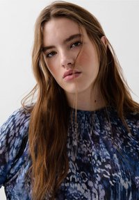 Multicolored blouse featuring a blue and purple abstract pattern, gathered neckline, and lightweight fabric with a flowing texture.