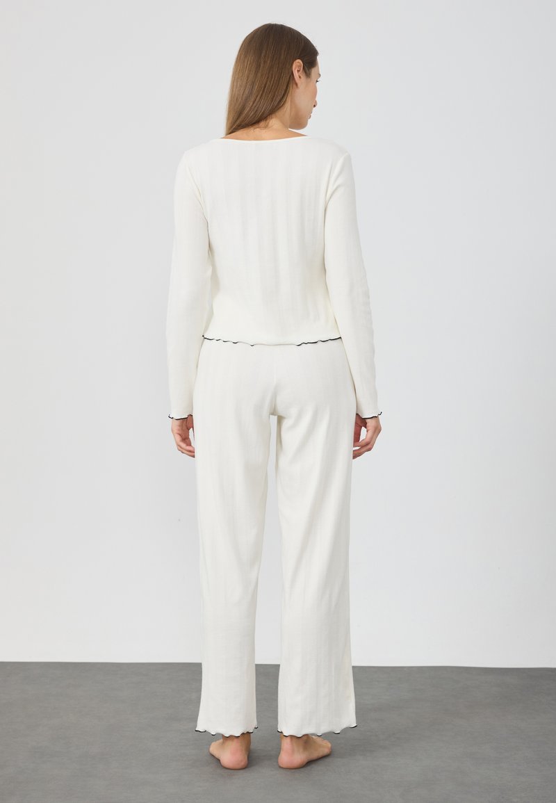 Ensemble de lounge blanc à côtes avec manches longues et bords festonnés. Pantalons amples au design décontracté. Texture douce, tissu léger.
