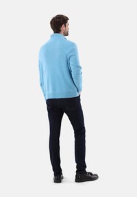 Helle blaue Strickpullover mit hohem Kragen, geripptem Saum und langen Ärmeln, kombiniert mit dunklen Jeans und schwarzen Schuhen.