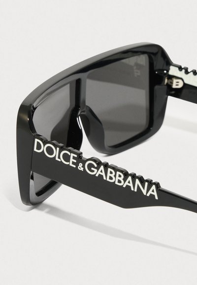 Mustad päikeseprillid paksu raami, hallide läätsede ja silmapaistva "DOLCE & GABBANA" brändinguga käsivarrel, millel on tekstuuriga aksendid.