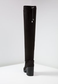 Botte noire au-dessus du genou en suède doux, avec un bout rond, un talon épais haut et un haut à cordon avec des accents métalliques.