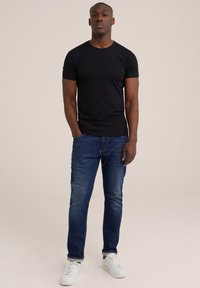 Zwart T-shirt met korte mouwen gecombineerd met blauwe spijkerbroek en witte sneakers. Eenvoudig ontwerp, aansluitende pasvorm en gladde textuur.