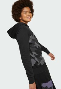 Svart hoodie med grå kamouflagemönster på framsidan, ribbad mudd och midja. Mjukt tyg med lös passform och en justerbar huva.