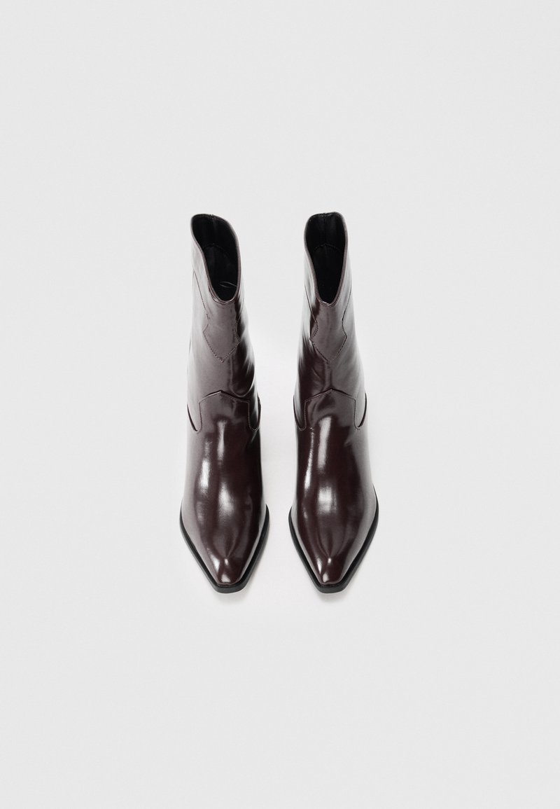 Stivaletti in pelle bordeaux con punta affusolata, finitura liscia e dettagli di cucitura discreti lungo il gambale. Suola nera piatta.