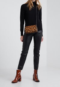 Sac bandoulière à imprimé léopard avec une chaîne, fabriqué en matériau texturé. Porté avec un pantalon en cuir noir ajusté et des bottines marron brillantes.