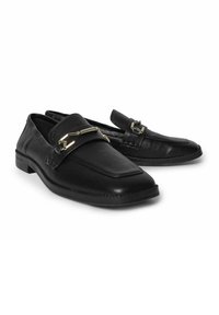 Black leather loafers with a flat heel, rectangular toe, decorative buckle detail, and stitched accents. Smooth texture with a polished finish.