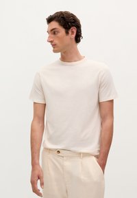 T-shirt corto a maniche corte color beige chiaro, con scollatura rotonda, realizzato in tessuto morbido. Abbinato a pantaloni color crema con dettaglio a bottoni.