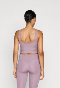 Sutien sport de culoare lavandă cu curele ajustabile și bandă lată. Material neted și elastic cu un design care se mulează pe corp, completat cu colanți asortați.