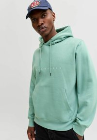 Minta zeleni dukserica s kapuljačom, kenguruh džepom, podesivim špagama i belim logotipom na prednjoj strani. Mekana tkanina i ležeran kroj.