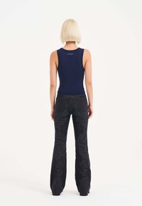 Marineblaues ärmelloses Oberteil mit tailliertem Design, kombiniert mit schwarzen Schlagjeans, die mit aufwendigen geprägten Mustern und Verzierungen an den Beinen versehen sind.