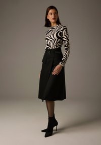 Long-sleeved top with black and white abstract pattern; paired with a high-waisted black skirt featuring pleats and belt; ankle booties.