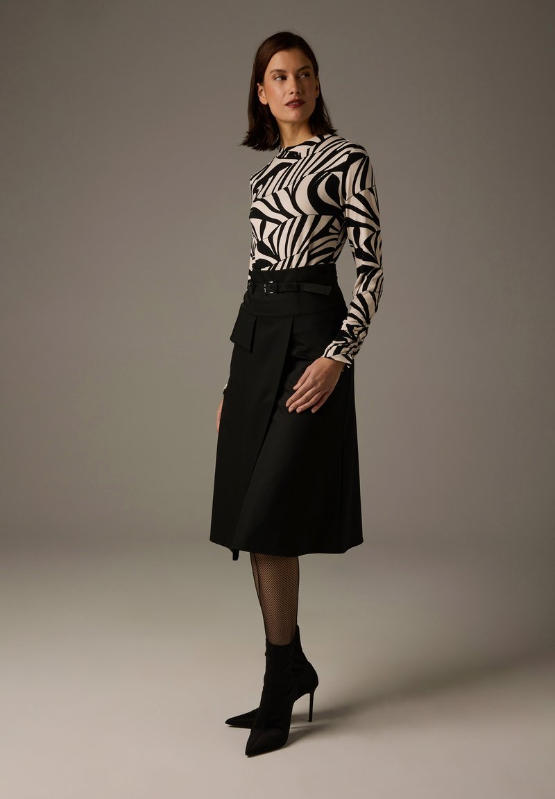 Long-sleeved top with black and white abstract pattern; paired with a high-waisted black skirt featuring pleats and belt; ankle booties.