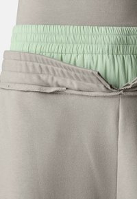 Grijze trui met een elastiche tailleband in muntgroen. De stof is zacht, met een licht gerimpelde textuur langs de naad van de tailleband.