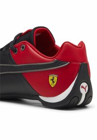 Černá a červená sportovní obuv se syntetickou kůží, která má texturovaný černý svršek, gumovou podrážku a logo Ferrari na patě.