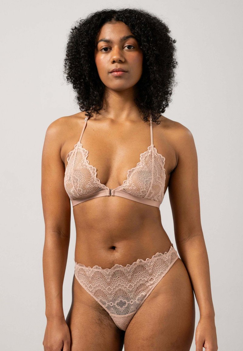 Kant bralette en bijpassende thong in een zachte nude kleur. De bralette heeft golvende randen en verstelbare bandjes; de thong heeft een kanten tailleband.