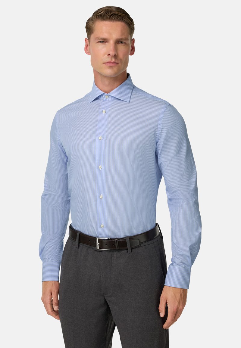 Gai zili krekli ar vertikālām svītrām, garām piedurknēm un klasisku apkakli. Saskaņots ar tumši pelēkiem biksēm un melnu jostu.