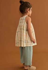 Leicht gemusterte ärmellose Bluse in Creme mit multicolor kariertem Design, kombiniert mit hellblauen strukturierten Hosen und beigen Schuhen.