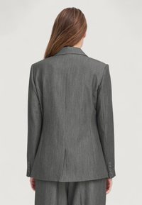 Giacca da abito grigia su misura con una texture che ricorda un fine tessuto di lana. Presenta un colletto a punta, una fessura posteriore e dettagli con cinque bottoni sui polsini.