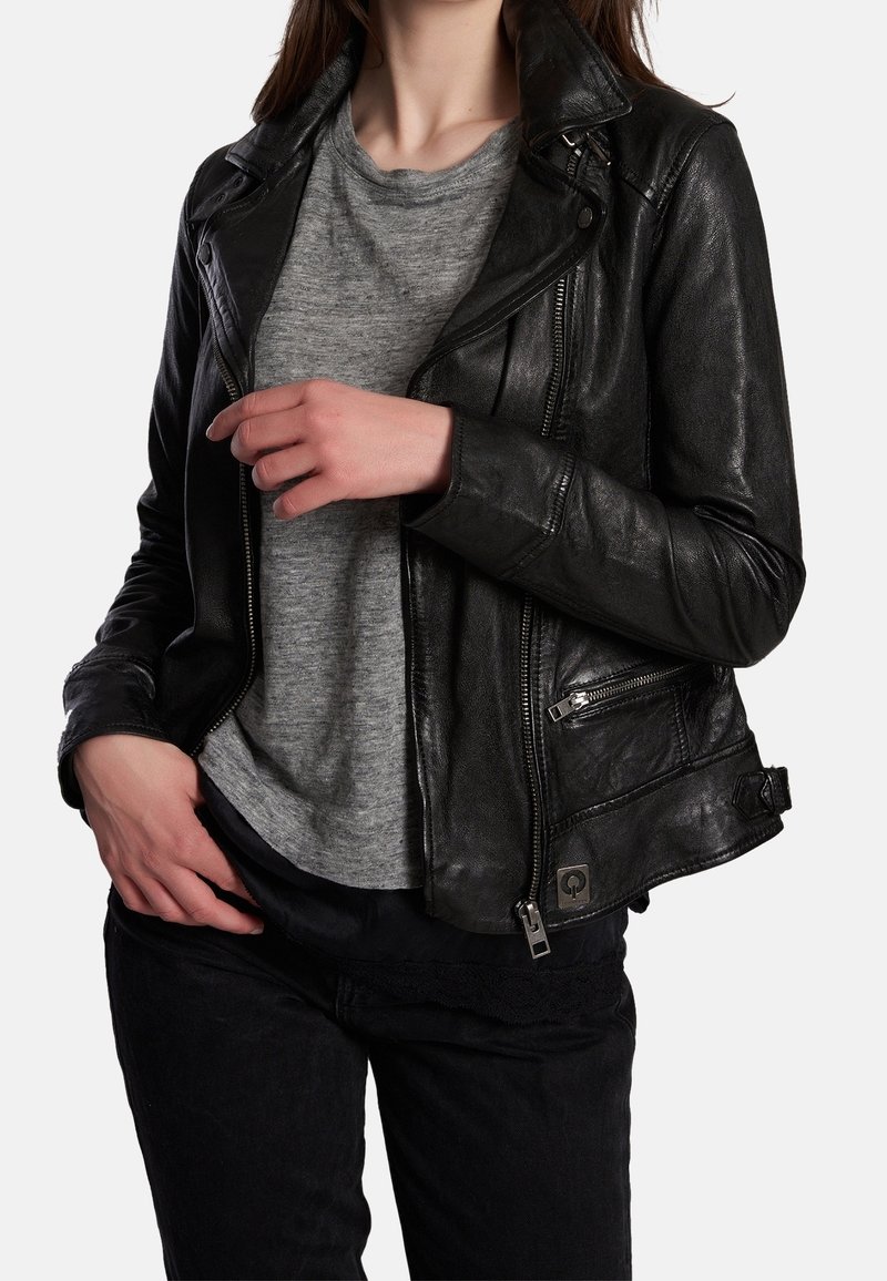 Svart skinn-mc-jacka med silverfärgade blixtlås, en knappkrage och fickor; bärs över en grå t-shirt och svarta byxor. Texturerad yta.