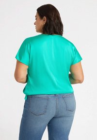 Kortärmad turkos topp med en mjuk textur; subtil sömdetalj på baksidan; tillsammans med blå jeans med två bakfickor.