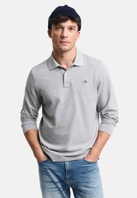Gray long-sleeve polo shirt with a collared neck, light texture, and subtle logo detail on the chest, paired with blue denim jeans.