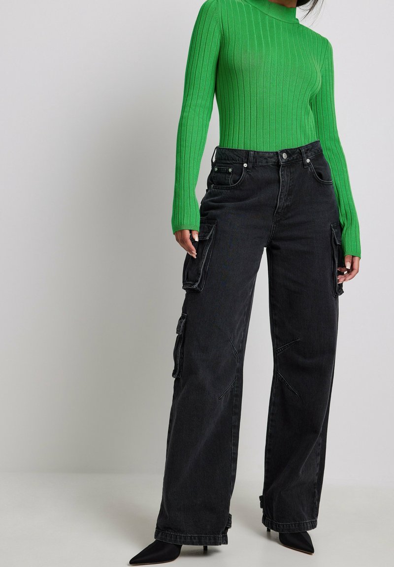 Haut vert à manches longues côtelé, associé à un pantalon cargo noir taille haute avec poches latérales et escarpins noirs à bout pointu.