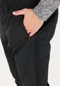 Svarta träningsbyxor med en ficka på sidan som kan stängas med dragkedja och en lätt, slät textur. Elastisk midja ger justerbarhet.