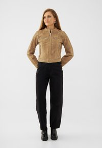 Tan läderjacka med en tight design, dragkedjefickor, axelsömnadsdetaljer, kombinerad med svarta byxor och ankelstövlar.