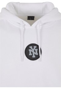 Felpa bianca con cappuccio e spessi lacci, un grande patch rotondo nero con il logo "NY" grigio, e una morbida texture in pile.